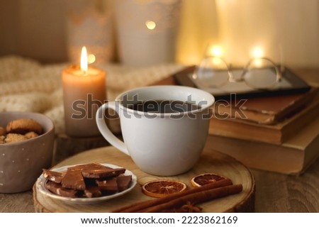 Bowl of cookies, cup of tea or coffee, chocolate, spices, knitted blanket, books, glasses and candle on the table. Cozy hygge atmosphere at home. Selective focus. Royalty-Free Stock Photo #2223862169