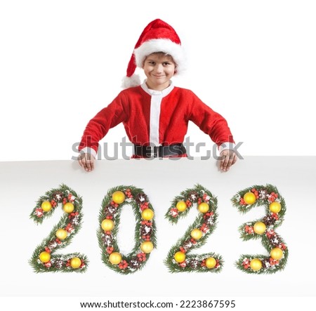 Boy Santa Claus is holding a christmas poster and 2023 number made by christmas tree branches isolated on white background