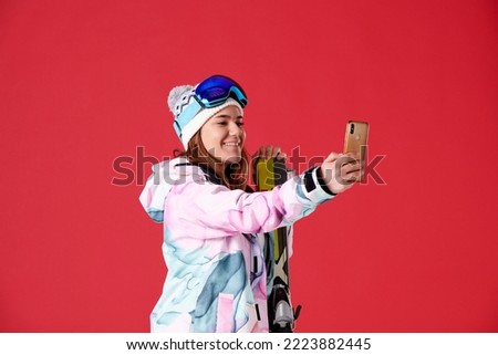 young woman in skis smiling taking a selfie on a red background