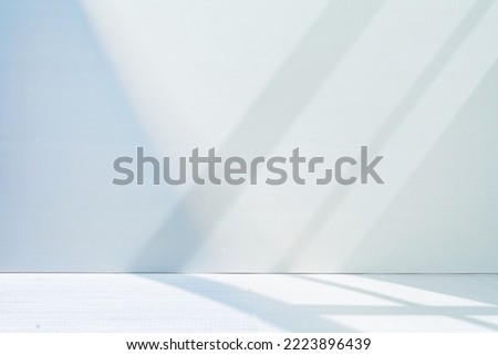 Light minimalist geometric background image in gray and light blue tones with light and shadow from window for product presentation.