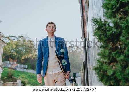 Smiling handsome young man businessman wearing suit messaging holding longboard walking street