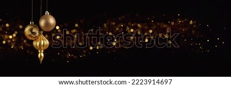 Christmas banner with three golden decoration balls on black background with bokeh lights with copy space. Wide panoramic header