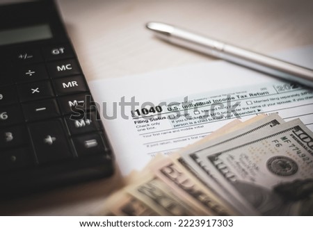 U.S. individual income tax return on a wooden table next to a calculator, dollars, money, a pen and a notepad. Blank US tax forms. Retro old style photo.