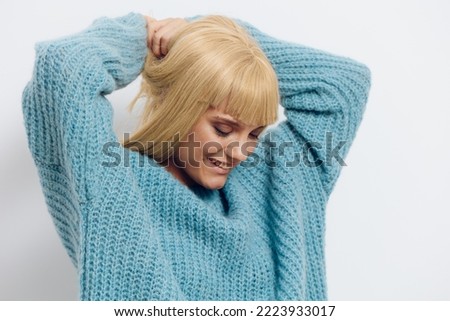  Horizontal photo, a woman on a white background in a blue sweater with beautiful blonde hair happily looks down with her hands behind her head