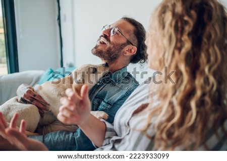 Beautiful happy family with dog talking and spending time together at home on a sofa. Couple petting their adopted puppy dog and relaxing at home on the weekend. Life with pets. Focus on a man and dog Royalty-Free Stock Photo #2223933099