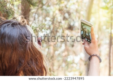 Close up of a young white woman wearing sunglasses taking a selfie with greenery out of focus in the background on a sunny day
