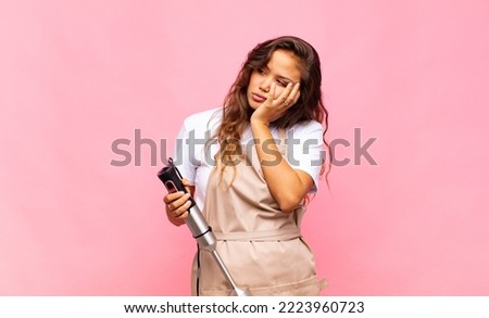 young woman baker feeling bored, frustrated and sleepy after a tiresome, dull and tedious task, holding face with hand