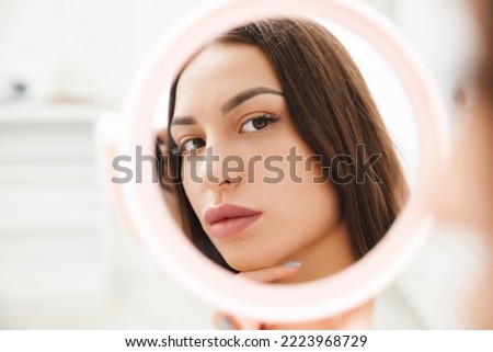 Portrait of a young brunette looking in the mirror. the reflection of a woman in the mirror. the girl admires her reflection in the mirror Royalty-Free Stock Photo #2223968729