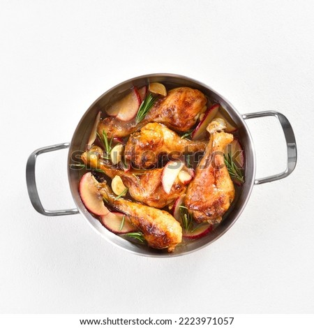 Chicken drumsticks baked with apples and herbs in stock pot over white background. Top view, flat lay