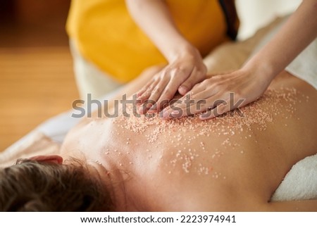 Masseuse massaging back of woman with salt scrub to get rid of dead skin cells Royalty-Free Stock Photo #2223974941