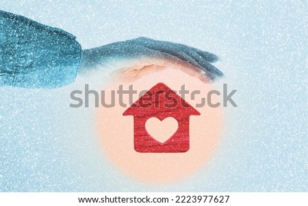 Heating of houses. A woman's hand protects a red little house with a heart in a warm round glow. Blue background with snow. The concept of insurance and property protection.