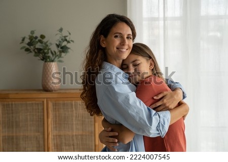 Young loving mother hugging cuddling with teen girl daughter at home and smiling at camera, expressing unconditional love. Mother-daughter friendship, happy motherhood, parenting of adolescent Royalty-Free Stock Photo #2224007545