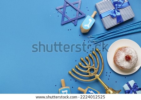 Plate with tasty doughnut, menorah, dreidels and gifts for Hanukkah celebration on blue background Royalty-Free Stock Photo #2224012525