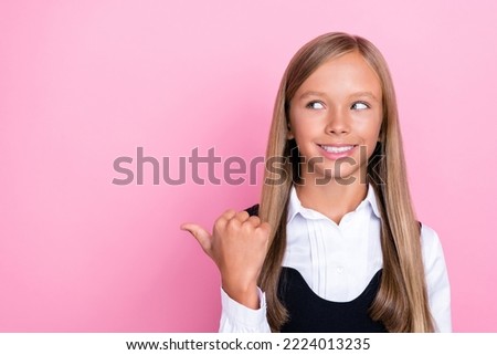 Closeup photo of young small schoolgirl wear uniform long hair blonde toothy smile finger point interested promo empty space isolated on pink color background