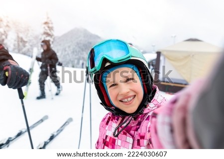 Active adorable school caucasian kid girl portrait enjoy have fun making selfie photo skiing in helmet, goggles winter extreme sport activities. Little child snowbarding luxury alpine resort mountain