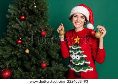 Photo of pretty adorable lady wear red sweater headwear smiling hanging tree decorations isolated green color background
