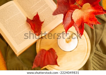 Glass of latte macchiato, open book, red autumn leaves and warm green scarf on the table. Sunday relaxing and still life.