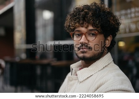 Portrait of pensive Indian man wearing eyeglasses looking at camera  on the street, copy space. Vision concept   Royalty-Free Stock Photo #2224058695