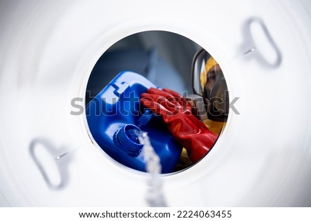 Inside barrel view of worker in protective suit mixing chemicals and making acids for industry. Royalty-Free Stock Photo #2224063455