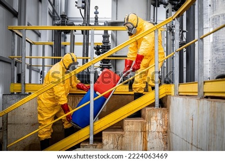 Workers in yellow protection suits and respiratory full face masks carrying aggressive substances or hazardous materials for chemical industry. Production of acids for industry. Royalty-Free Stock Photo #2224063469