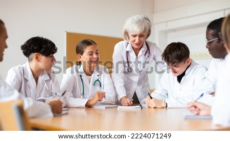 Group of medical workers in white coats sitting around desk during professional training course, listening to experienced aged female lecturer Royalty-Free Stock Photo #2224071249