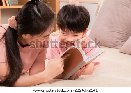 Asian happy elementary school kid and single mom spend free time reading a book and tease in holiday. Beautiful mother telling fairy tale stories to adorable son laying on bed, parenthood relationship