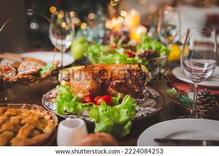 Traditional celebration. Roasted chicken, wine, vegetables salad and various food are set on table for family to celebrate together at night and Christmas tree set in the room for Christmas holiday. Royalty-Free Stock Photo #2224084253
