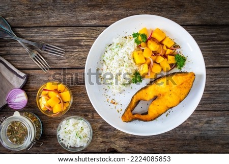 Fish dish - fried halibut with white boiled rice and avocado on wooden table 