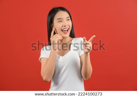 Portrait of young asian woman pointing with two hands and fingers to the side over isolated red background. Advertising and lifestyle concept.