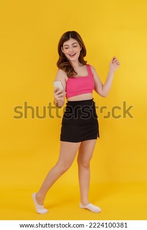 Portrait of Smiling young woman selfie with mobile phone in her hands while standing isolated over yellow background. Technology and lifestyle concept.