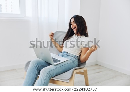 A woman relaxing at home sitting on a chair and playing games on her laptop, a smile of happiness and the joy of victory