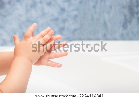 Closeup of a child's soapy hands being washed under running water in a sink.