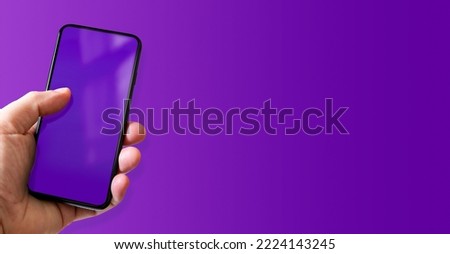 Hand holding a smartphone with blank purple screen. Colorful background. Horizontal banner.