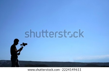 Videographer filming Carpathian mountains landscape. Man using steadicam and camera to make footage. Video shoot. videographer holds the camera with a big lens mounted on a stabilization gimbal
