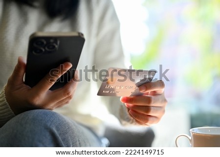 Young Asian woman holding her smart mobile phone and her credit card while sitting in the cafe. online shopping concept. close-up hands image