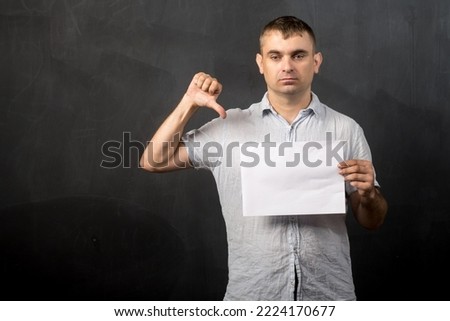 a man of European appearance stands with a sheet of paper and shows his finger down. place for text