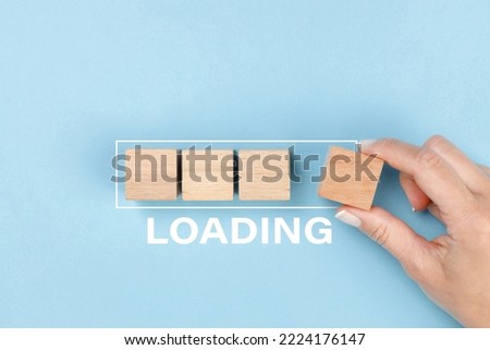 Hand putting wooden blocks in progress bar on blue background with the word Loading. Loading, reboot, refresh or mindset concept.  Royalty-Free Stock Photo #2224176147