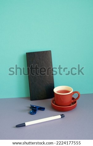 Notebook, pen, clip, cup of tea on purple desk. blue background. workspace