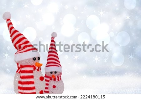 Christmas greeting card template. Xmas background texture with two cute winter snowman with red white striped hat and scarf in a abstract snowy winter landscape. Space.