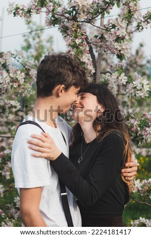 Beautiful strong love between two young people walking under apple trees. Candid portrait of a couple in casual clothes. Smile of a young couple.