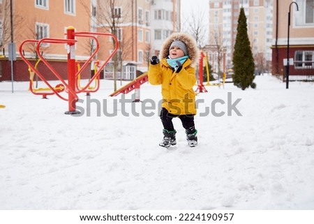 Happy child having fun in the snow in the city. Winter fun outside. Boy in bright orange winter Jacket. Winter holidays concept.
