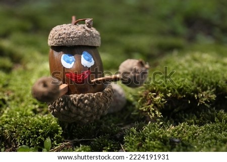 Cute figure made of acorns on green moss outdoors, closeup