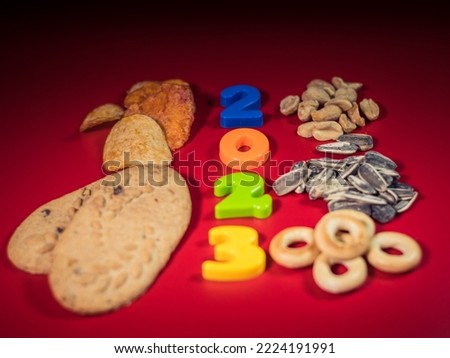 New Year's numbers on the table 2023 and snacks cookies, nuts, sunflower seeds on a red background.