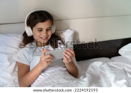 Girl of 10 years communicates with friends via video call. Teens wins a game on the phone at the desk at home in the living room. Happy adult child listens to music, plays games, studies with lessons