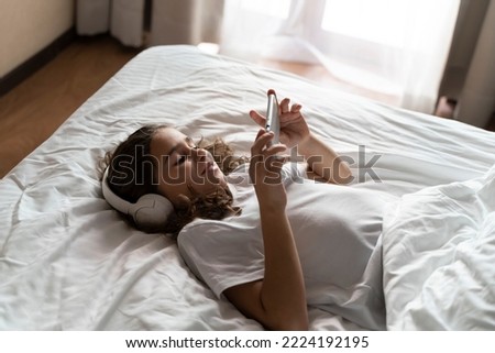 Girl wins a game on the phone at the desk at home in the bed room. Happy adult child wakes up and listens to music, plays games, studies with lessons on the phone