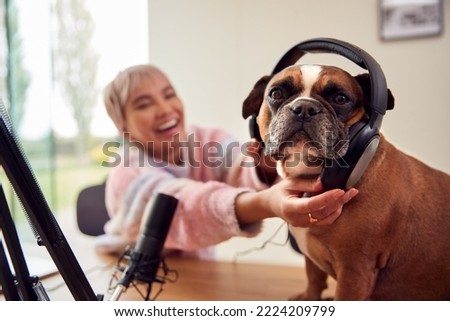 Woman With Pet French Bulldog Wearing Headphones Recording Podcast Or Broadcasting On Radio At Home