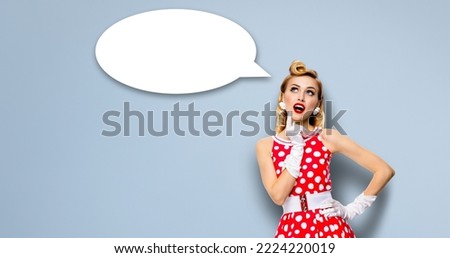 Studio portrait image of thinking woman in red pin up dress. Blond pinup thougthfull girl over grey background. White empty blank speech sign bubble, having idea. Mockup, ready for your design. Ad.