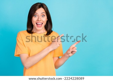 Photo of optimistic astonished girl straight hair yellow t-shirt directing empty space open mouth isolated on blue color background