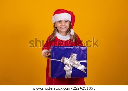 Funny smiling child girl in Santa Claus red hat holding Christmas gift in hand. Christmas concept.