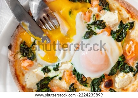 Pizza with fried egg, shrimps, cheese and spinach in a plate on a white table with cutlery